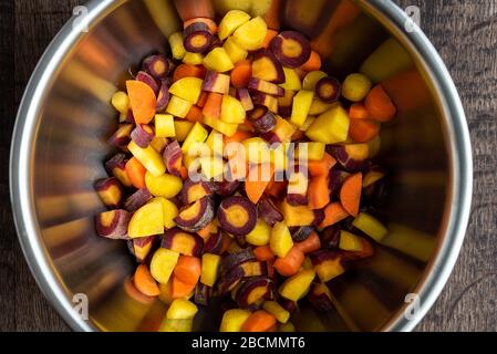 Carottes arc-en-ciel coupées en dés dans un bol en acier inoxydable, sur une table en bois Banque D'Images