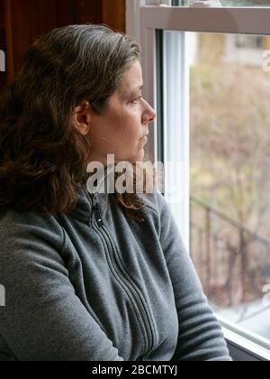 Oak Park, Illinois, États-Unis. 4 avril 2020. Une femme regarde sa fenêtre de cuisine pendant COVID-19 abri-dans-ordre. Être coincé à la maison peut apporter des sentiments d'isolement et de solitude. Banque D'Images