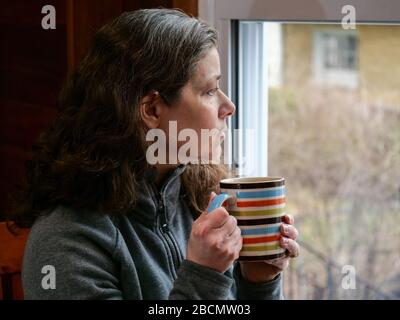 Oak Park, Illinois, États-Unis. 4 avril 2020. Une femme regarde sa fenêtre de cuisine pendant COVID-19 abri-dans-ordre. Être coincé à la maison peut apporter des sentiments d'isolement et de solitude. Banque D'Images