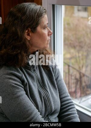 Oak Park, Illinois, États-Unis. 4 avril 2020. Une femme regarde sa fenêtre de cuisine pendant COVID-19 abri-dans-ordre. Être coincé à la maison peut apporter des sentiments d'isolement et de solitude. Banque D'Images