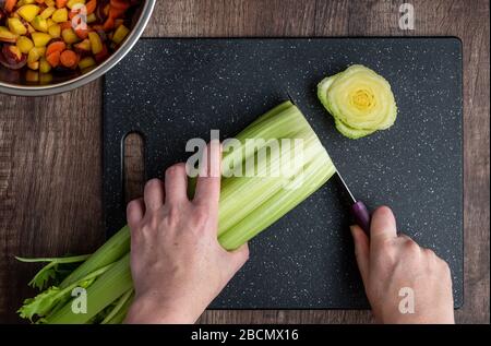 Les mains de la femme coupent un groupe de céleri, de planche à découper noire et de couteau de chef Banque D'Images