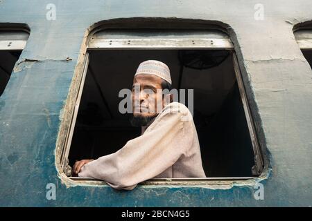 Dhaka / Bangladesh - 19 janvier 2019: Homme musulman avec barbe portant des vêtements musulmans blancs traditionnels et pose de chapeau dans une fenêtre de train à Dhaka train s Banque D'Images