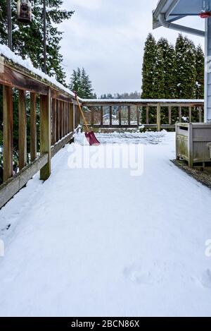 Neige fraîche et humide sur une terrasse en cèdre, avec pelle à neige, vue sur le quartier enneigé Banque D'Images