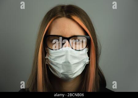 Femme intelligente dans les lunettes portant un masque médical. Jeune femme dans le masque chirurgical en toile de fond gris foncé. Concept d'hygiène personnelle, protection aga Banque D'Images
