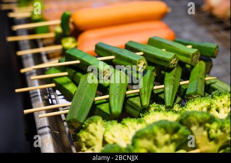 Brocoli et carotte sur brochettes pour barbecue sur le marché alimentaire en Thaïlande. Cuisine asiatique populaire. Photo prise en basse lumière la nuit Banque D'Images