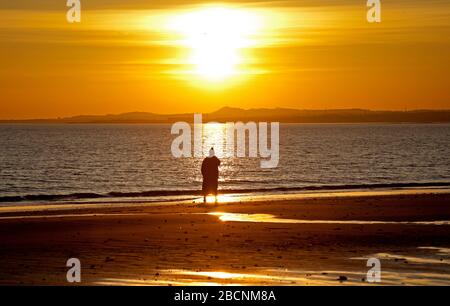 Portobello, Édimbourg, Écosse, Royaume-Uni. 5th avril 2020. Lever du soleil sur la plage de Portobello, avec diverses personnes photographiés nager, marcher, courir et s'asseoir dans la contemplation sur la plage de sable. Banque D'Images