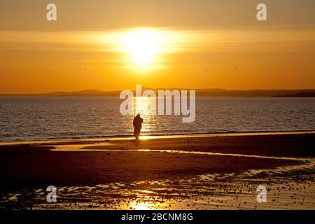 Portobello, Édimbourg, Écosse, Royaume-Uni. 5th avril 2020. Lever du soleil sur la plage de Portobello, avec diverses personnes photographiés, marcher, nager, courir et s'asseoir dans la contemplation sur la plage de sable. Banque D'Images