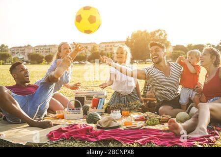 Les familles heureuses qui font un pique-nique dans le parc de la ville - les jeunes parents s'amusent avec leurs enfants en été en mangeant, en buvant et en riant ensemble - Love A. Banque D'Images