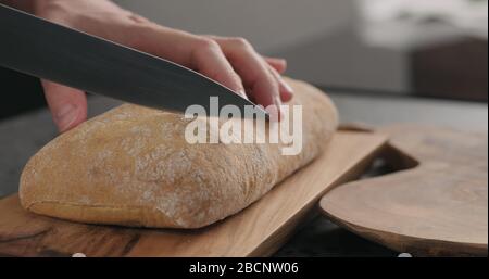 homme en tranches de ciabatta avec un couteau à pain sur une planche à olives Banque D'Images