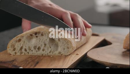 homme en tranches de ciabatta avec un couteau à pain sur une planche à olives Banque D'Images