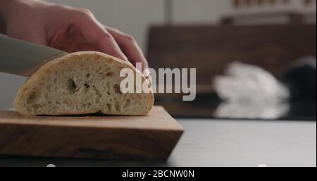 homme trancheuse hier ciabatta avec couteau à pain sur planche à olives Banque D'Images