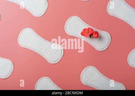 Tampons hygiéniques sur fond rose sous forme de répétitions diagonales, avec une fleur rouge sur le tampon. Banque D'Images