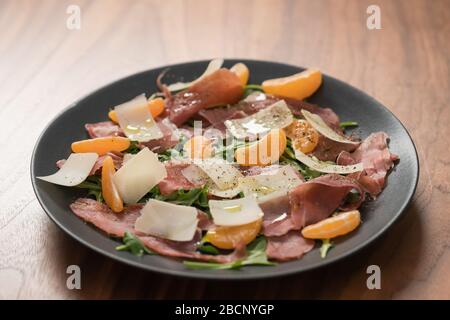 Salade avec prosciutto, mandarines et fromage d'époque sur table en noyer Banque D'Images