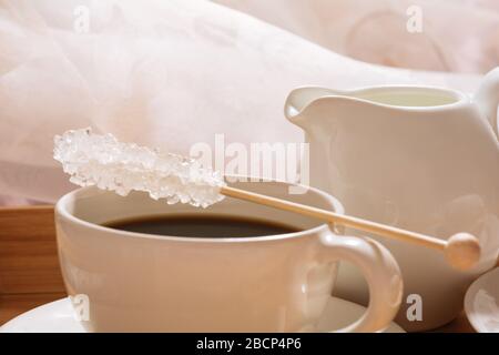 Une tasse de café fraîchement moulu et chaud le matin avec du sucre cristal sur un bâton et un pichet de lait froid. Banque D'Images