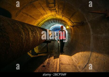 Le travailleur du tunnel examine le pipeline dans le tunnel souterrain. Banque D'Images