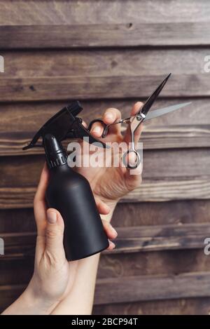 Outils de coiffure sur un fond en bois dans les mains d'un maître. Spray de protection et ciseaux à cheveux. Des outils de coiffure professionnels. Banque D'Images