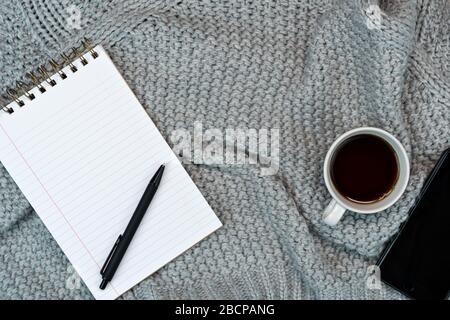 Un espace de travail confortable avec un café chaud, du papier à note et un smartphone. Travaillez à domicile. Écriture. Concept chaud par temps froid. Banque D'Images