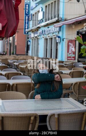 Jeune femme sérieuse avec masque protecteur assis à l'extérieur sur la terrasse vide du café et toussant pendant l'éclosion de coronavirus Banque D'Images