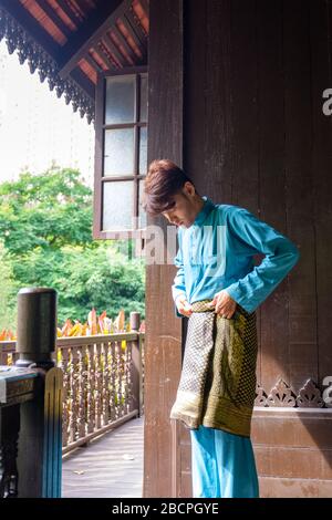 Malay homme portent un tissu traditionnel et ajuste son songket samping à la maison traditionnelle en bois. Banque D'Images