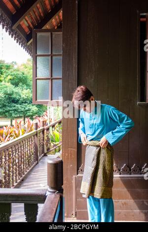 Malay homme portent un tissu traditionnel et ajuste son songket samping à la maison traditionnelle en bois. Banque D'Images