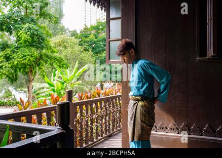 Malay homme portent un tissu traditionnel et ajuste son songket samping à la maison traditionnelle en bois. Banque D'Images