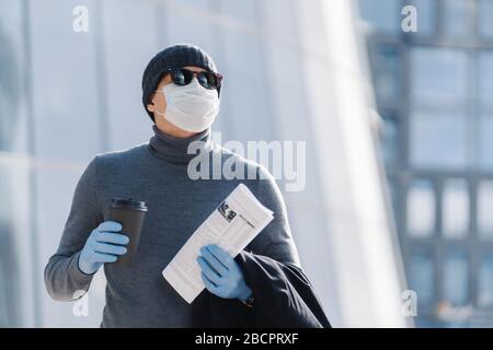 La prise de vue horizontale du jeune homme dans le masque médical empêche la pneumonie infectieuse, la pandémie de coronavirus, l'épidémie de virus, boit du café à emporter, va travailler, Banque D'Images