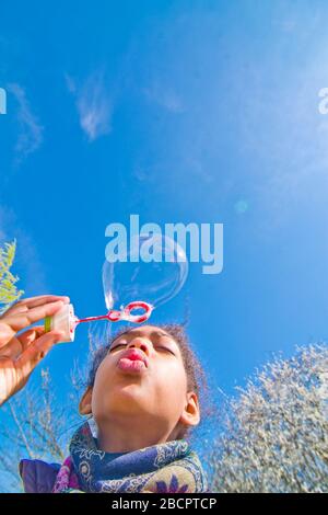 une jeune fille heureuse crée des bulles de savon colorées dans le ciel bleu Banque D'Images