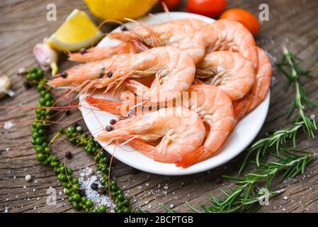 crevettes fraîches sur la plaque blanche avec ingrédients herbes et épices / cuisson fruits de mer crevettes servies sur une table en bois fond Banque D'Images