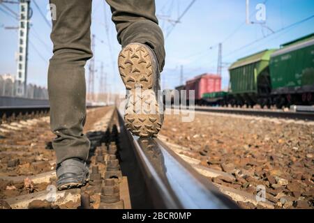 Semelle de chaussures près des rails. Le tramp de rue dans les jeans sales marche le long des voies de chemin de fer contre le fond des trains Banque D'Images