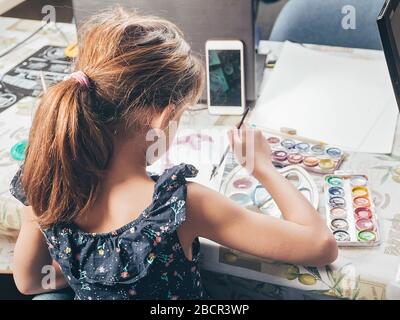 Fille dessine avec des peintures. Idées d'activités avec des enfants à la maison. Prise de vue verticale. Vue de derrière Banque D'Images