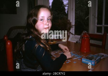 Jeune fille portant des salopettes rayées Big Smith assis à une table faisant un puzzle, Royaume-Uni 1973 Banque D'Images