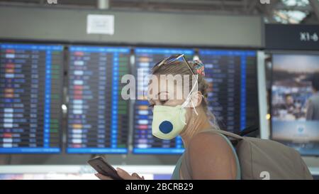 Femme caucasienne à l'aéroport de Suvarnabhumi avec masque médical protecteur. Carte d'information de vol. Utilisez un smartphone mobile. Cov-2-SRAS-19. Banque D'Images