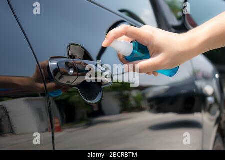 La main de la femme vaporise de l'alcool, du désinfectant vaporisateur sur la poignée de la porte de la voiture. Prévenir l'infection de Coronavirus, Covid-19. Banque D'Images