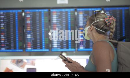 Femme caucasienne à l'aéroport de Suvarnabhumi avec masque médical protecteur. Carte d'information de vol. Utilisez un smartphone mobile. Cov-2-SRAS-19. Banque D'Images