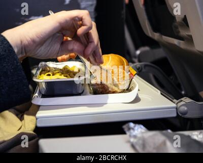 Femme tenant la fourche et le couteau manger un délicieux repas dans la classe affaires économique moderne d'avion pendant le long vol transatlantique Banque D'Images