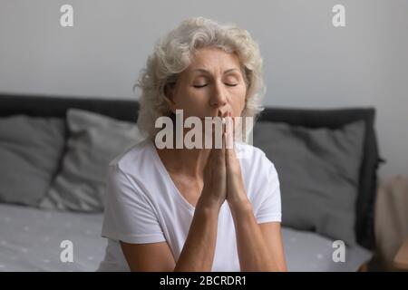 Paisible femme d'âge moyen priant Dieu le matin après le réveil. Banque D'Images