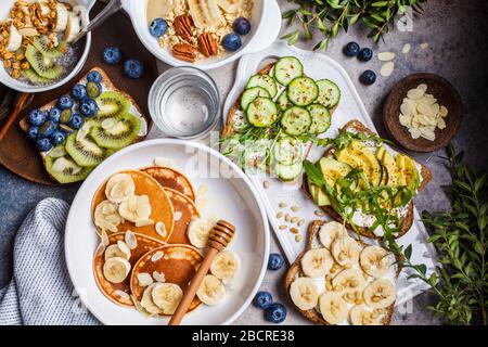 Table de petit-déjeuner végétarien saine et variée. Flocons d'avoine avec fruits, pudding de chia, crêpes avec banane et miel et toasts avec fruits, légumes et cr Banque D'Images