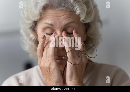 Femme fatiguée à maturité frottant le pont de nez après avoir retiré des lunettes. Banque D'Images