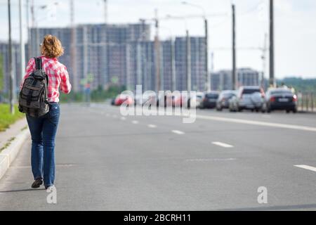 Vue arrière à Caucasien femme Hitchhiker marchant sur la route d'asphalte dans la rue urbaine, copyspace Banque D'Images