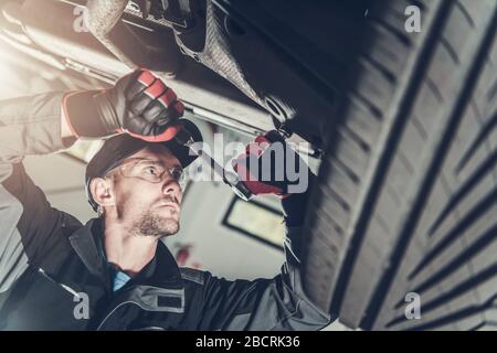 Entretien de la suspension automobile moderne. Technicien automobile caucasien dans ses 30 s fixant les éléments de suspension du véhicule. Banque D'Images