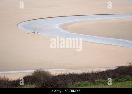 Une famille avec leur chien social distancing qui la rivière Gannel coule dans la mer à Crantock Beach, près de Newquay, Cornwall Banque D'Images