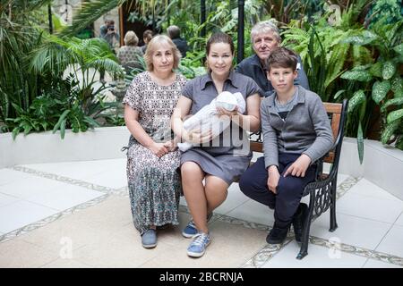 Père faire une photo avec sa famille assise sur un banc avec le nouveau-né, la femme adulte porte un enfant dans les bras, le fils et les grands-parents sont autour Banque D'Images