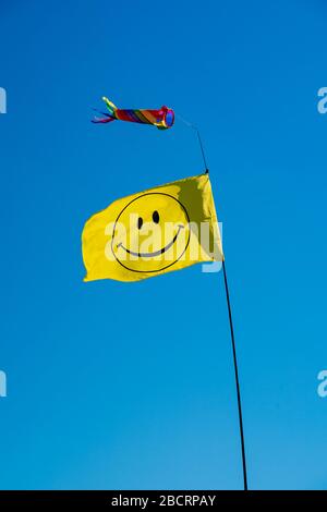 Mât télescopique avec un drapeau smiley jaune et une chaussette à vent colorée contre le ciel bleu. Perry Green, beaucoup Hadham, Hertfordshire Banque D'Images
