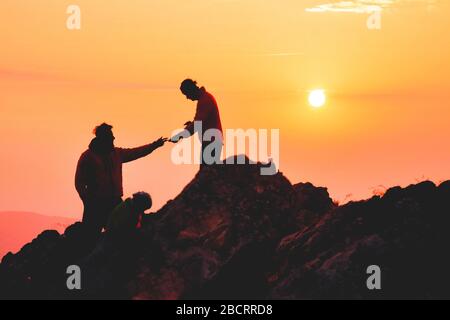 Deux amis s'aident les uns les autres et avec le travail d'équipe essayant d'atteindre le sommet de la montagne pendant le merveilleux lever du soleil d'été. Banque D'Images
