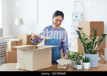 Taille vers le haut portrait de la jeune femme asiatique emballage ou déballage carton boîte et sourire heureux tout en se déplaçant dans la nouvelle maison, espace de copie Banque D'Images