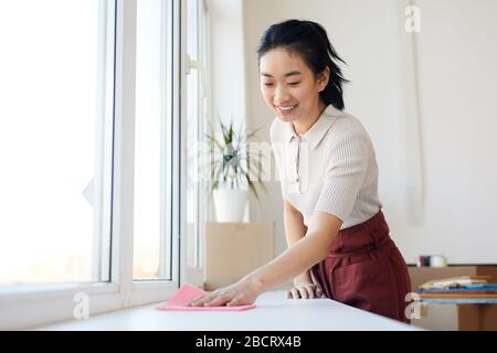 Taille vers le haut portrait de la jeune femme asiatique essuyant will tout en profitant de nettoyage de printemps dans la maison ou l'appartement, espace de copie Banque D'Images