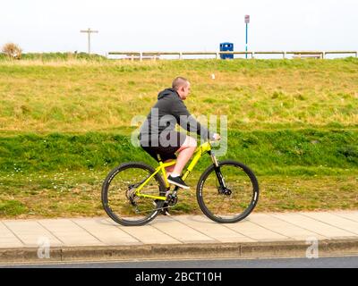 Un jeune homme qui monte un vélo tout-terrain jaune sur une piste cyclable avec une rive herbacée derrière lui Banque D'Images