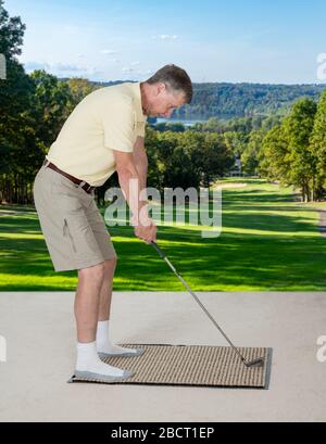 Homme caucasien senior pratiquant sa poignée de golf et swing sur un tapis dans la chambre à la maison et imaginant qu'il était dehors sur un vrai terrain de golf Banque D'Images