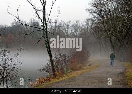 Un homme marche seul dans l'inconnu brumeux sur un chemin de forêt malteuse à côté d'un lac, une métaphore pour l'actuel distancement social Banque D'Images