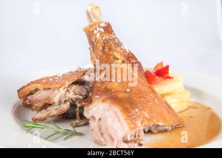 Jambe de chèvre rôtie avec tranches de pommes de terre cuites au four. Banque D'Images